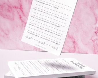 May include: A white notepad with the title "Cognitive Restructuring" and a series of questions to help with cognitive restructuring. The notepad is on a pink marble background.