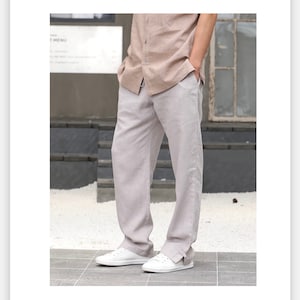 May include: A pair of light gray linen pants with a relaxed fit and a slightly cuffed hem. The pants are worn with a light brown linen shirt and white sneakers.