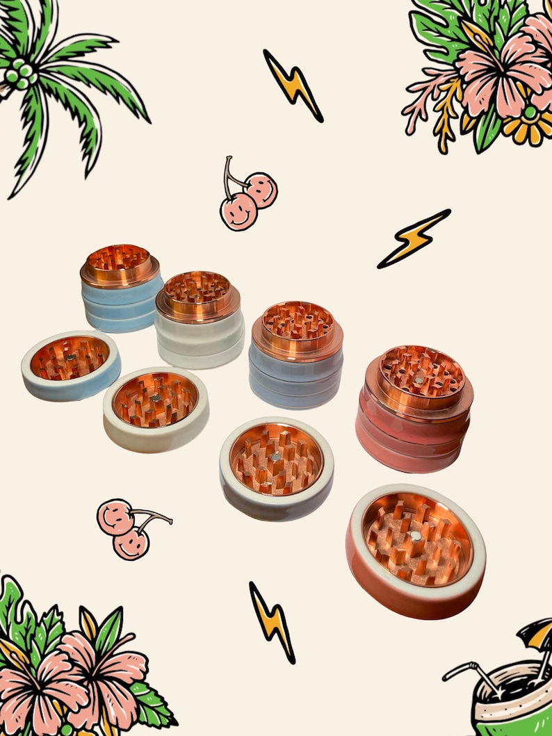 May include: A collection of herb grinders featuring metallic copper-coloured teeth and smooth, matte-finished exterior shells in shades of light blue, white, grey, and pink, arranged in a scattered pattern against a light background.