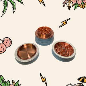 May include: A three-piece herb grinder featuring a metallic copper interior with sharp teeth and a smooth, light blue exterior casing. The set is displayed in three separate components, showing the top, middle, and bottom sections of the device.