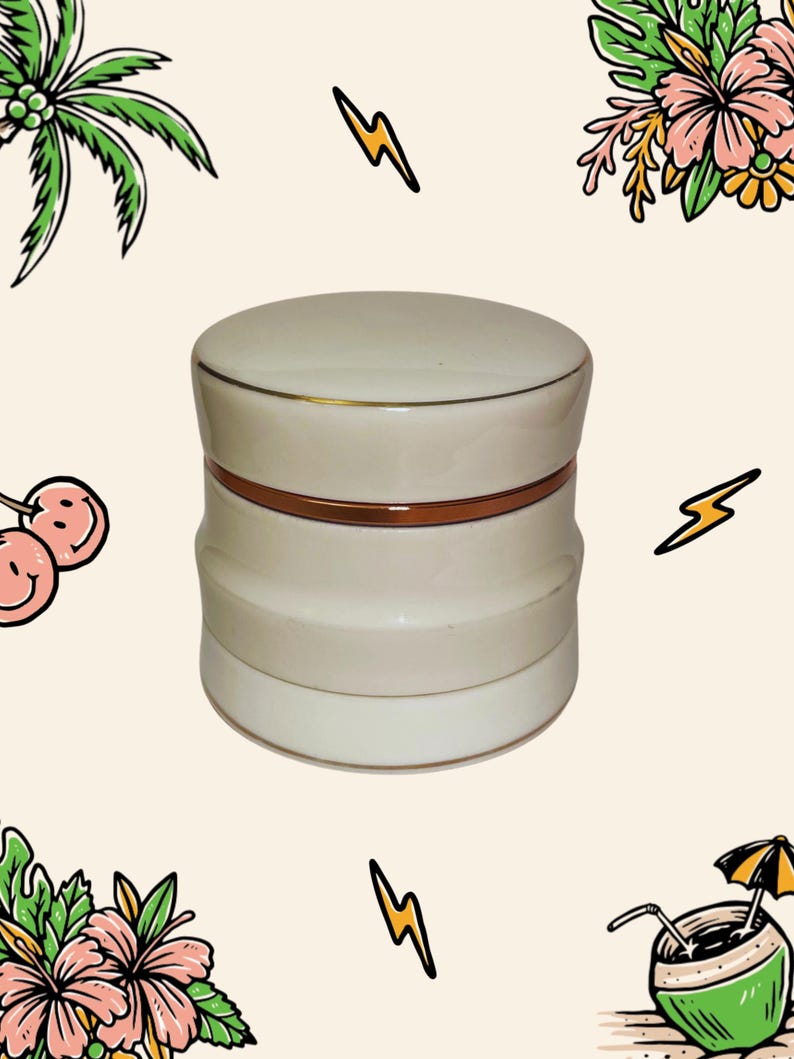 May include: A cylindrical off-white ceramic jar with a matching lid, featuring a smooth finish and a thin, metallic copper-coloured band encircling the centre where the lid meets the base. The container has a slightly indented middle section.