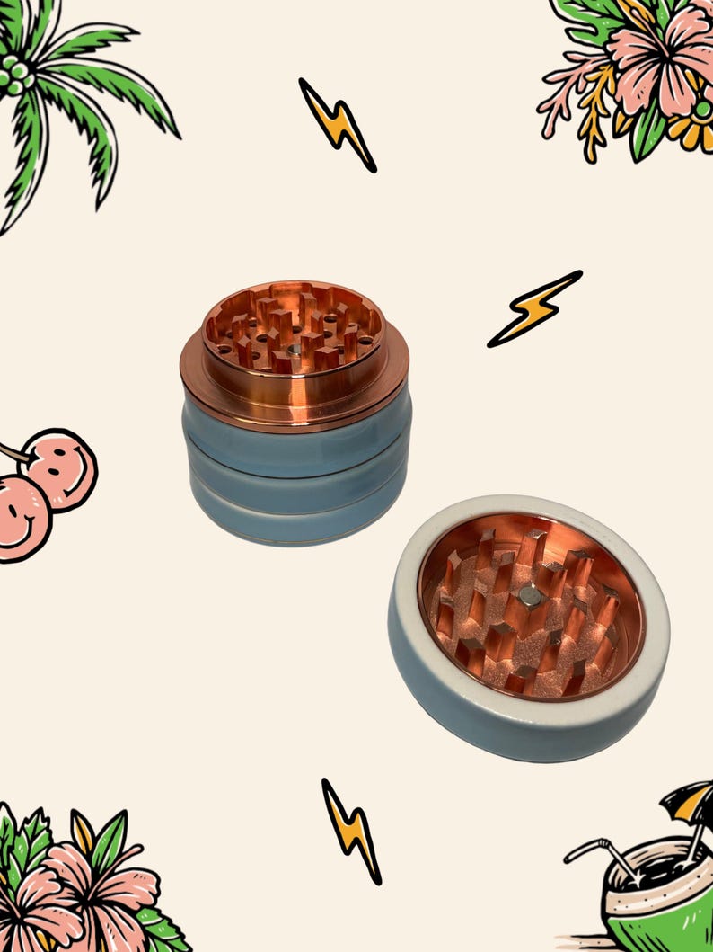 May include: A multi-part herb grinder featuring a light blue exterior and a metallic copper interior with sharp, diamond-shaped teeth. The device consists of a stacked cylindrical base and a separate lid, both showing the copper grinding mechanism.
