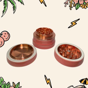 May include: A three-piece herb grinder with a metallic copper interior and a smooth, matte coral-pink exterior. The set includes a base, a middle section with sharp teeth, and a top lid, all featuring a consistent circular design and finish.