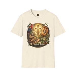 Pode incluir: Camiseta creme com um gráfico circular que apresenta uma cruz, um leão, uma cobra, uma arara e um sapo. O gráfico é rodeado por folhagens e inclui o texto "ALL CREATION TESTIFIES" e "PSALM 19:1".