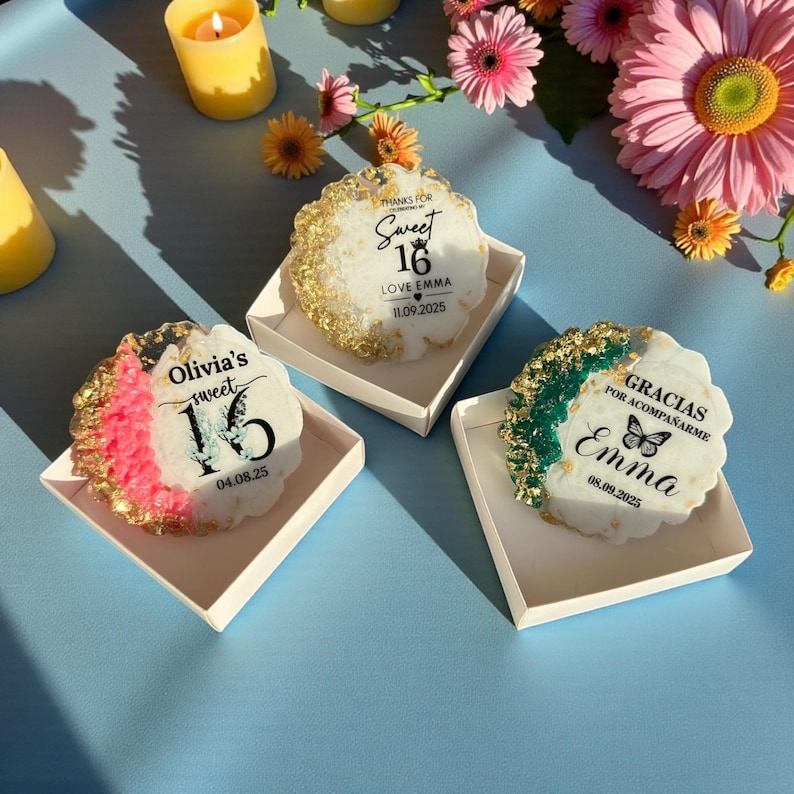 May include: Three decorative resin coasters with gold leaf accents, each in a white box. One coaster reads "Sweet 16" with a date. Another says "Olivia's sweet 16" with a date. The third says "Gracias por acompa&ntilde;arme Emma" with a date.