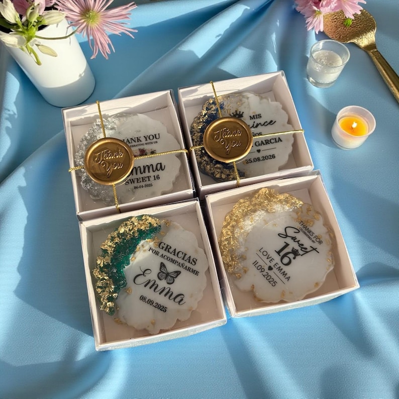 May include: Four white gift boxes with decorative cookies. Each cookie has a unique design with gold accents and personalized text, including "Thank You," names, and dates. The boxes are tied with gold twine.