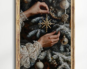 May include: A framed print depicts a person's hands delicately placing a gold snowflake ornament on a snow-covered Christmas tree. The artwork features gold and white ornaments, and a wooden frame.