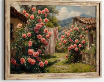 May include: A framed print of a picturesque garden scene. Lush pink rose bushes bloom around rustic buildings with terracotta roofs. Laundry hangs on a clothesline, and a path leads into the distance, with mountains in the background.
