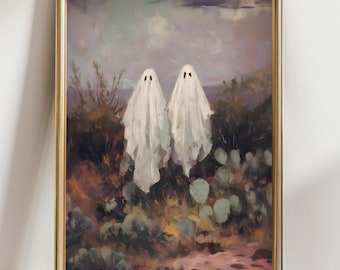 May include: A framed art print featuring two white ghost figures with black eye slits, set against a backdrop of desert flora and a cloudy sky. The artwork is in a gold-colored frame, evoking a vintage aesthetic.