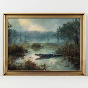 May include: A framed landscape painting depicts a swamp scene with an alligator in the water. The artwork features a gold frame and a misty, atmospheric setting with trees and vegetation. The color palette includes greens, blues, and browns.