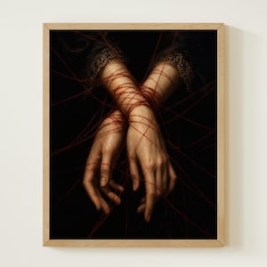 May include: A framed wall art print featuring two hands crossed at the wrists, wrapped in thin red string against a dark black background. The wrists are adorned with dark lace cuffs with gold trim, and the red string extends outward in lines.