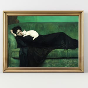 May include: A framed print of a woman in a black dress reclining on a green sofa with a white cat. The artwork has a gold frame and a green background. The woman is resting her head on her hand.
