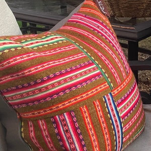 May include: A brown, multi-colored striped throw pillow with a woven design. The pillow has a tag that says "KE-D" on it.
