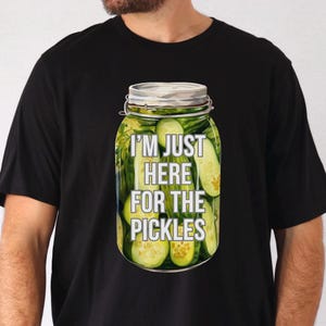 May include: A black t-shirt with a graphic of a jar of pickles. The text on the jar reads "I'm just here for the pickles."