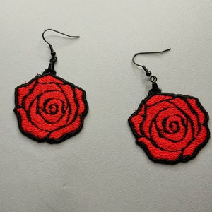 Könnte beinhalten: Ein Paar rote Rosenohrringe mit schwarzen Drahtösen. Die Rosen sind mit rotem Garn gestickt und mit schwarzem Garn umrandet.