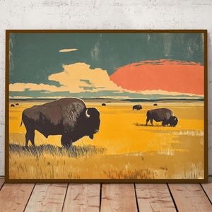 May include: A framed art print featuring a stylized landscape with a large dark brown bison in the foreground and smaller bison grazing in a golden yellow prairie. The sky displays a deep teal blue upper section and a large orange sun.
