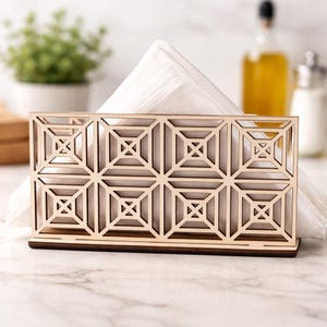 May include: A wooden napkin holder with a geometric design. The holder is made of light-colored wood and features a repeating square pattern. White napkins are visible inside the holder. The holder sits on a marble surface.