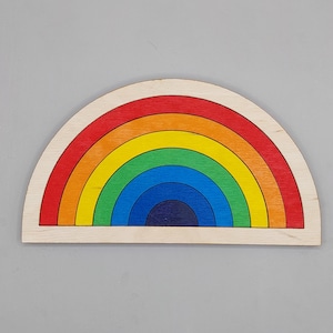 Pode incluir: Quebra-cabeça de arco-íris de madeira com arcos vermelhos, laranja, amarelo, verde, azul e índigo. O brinquedo é feito de madeira natural com um acabamento liso. O arco-íris tem formato de semicírculo, para crianças.