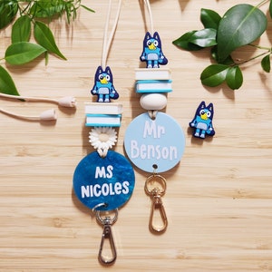 Pu&ograve; includere: Due lacci blu e bianchi con un personaggio di cane cartone animato blu, un ciondolo a forma di fiore bianco e un'etichetta rotonda blu e bianca. Le etichette del nome recitano "Ms. Nicoles" e "Mr. Benson".