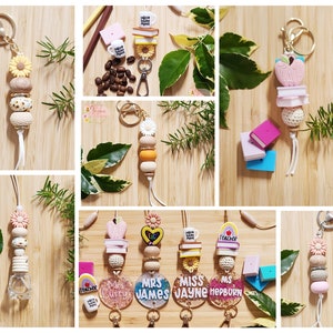 Pu&ograve; includere: Una collezione di ciondoli colorati per portachiavi da insegnante con vari design, tra cui libri, tazze da caff&egrave;, fiori ed etichette con nomi personalizzati. I ciondoli sono infilati su cordini bianchi con anelli portachiavi dorati.