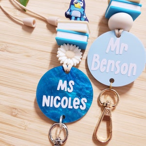Pu&ograve; includere: Due lacci per badge da insegnante blu e bianco con un ciondolo a forma di cane blu, un ciondolo a forma di margherita bianca e un ciondolo a forma di libro blu e bianco. I lacci hanno un cerchio blu con testo bianco che recita "Ms. Nicoles" e un cerchio blu chiaro con testo bianco che recita "Mr. Benson".