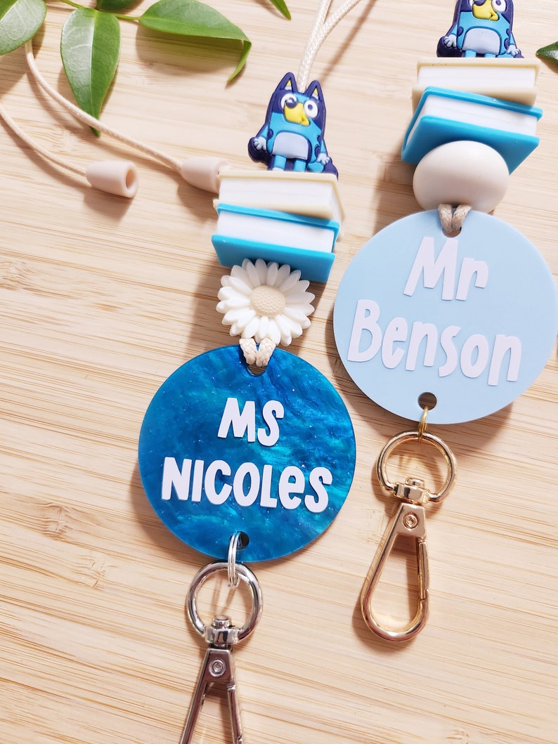 Pu&ograve; includere: Due lacci per badge da insegnante blu e bianco con un ciondolo a forma di cane blu, un ciondolo a forma di margherita bianca e un ciondolo a forma di libro blu e bianco. I lacci hanno un cerchio blu con testo bianco che recita "Ms. Nicoles" e un cerchio blu chiaro con testo bianco che recita "Mr. Benson".