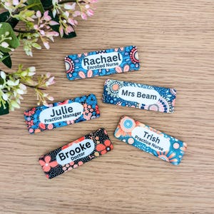 May include: Five colourful name tags with an aboriginal art design. The name tags read "Julie Practice Manager", "Rachael Enrolled Nurse", "Mrs Beam", "Brooke Doctor", and "Trish Practice Nurse".