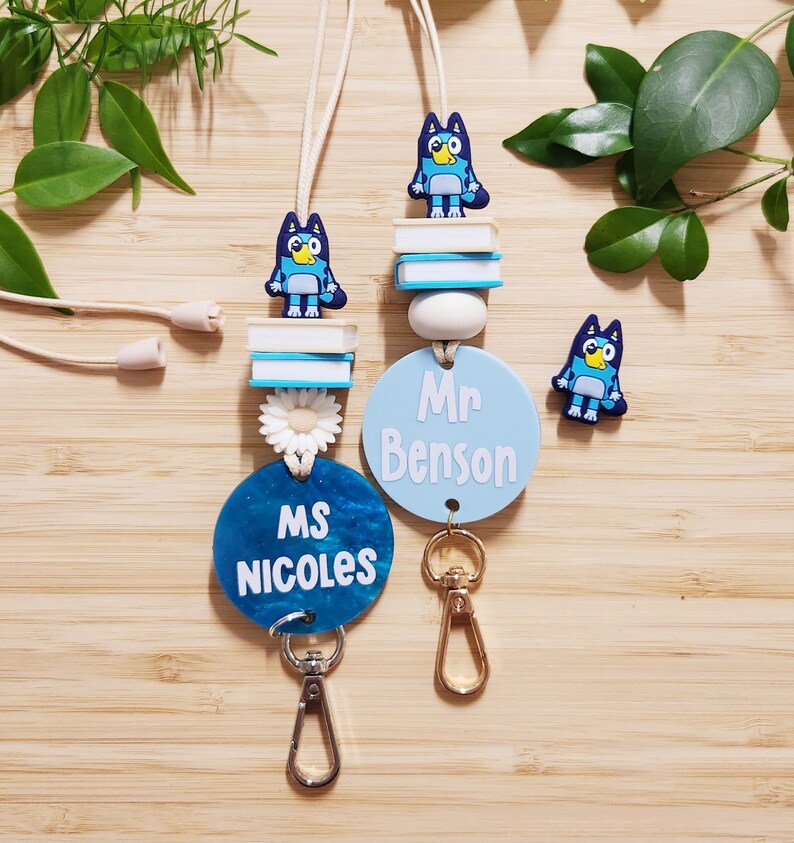 Pu&ograve; includere: Due lacci blu e bianchi con un personaggio di cane cartone animato blu, un ciondolo a forma di fiore bianco e un'etichetta rotonda blu e bianca. Le etichette del nome recitano "Ms. Nicoles" e "Mr. Benson".