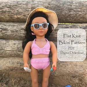 May include: A pink knitted bikini for a doll, with a matching hat and sunglasses. The doll is sitting on a blue towel on a sandy beach. The text "Flat Knit Bikini Pattern PDF Digital Download" is on a white sign. The text "Sara's Simple Knits" is on a green and white sign.