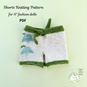 Könnte beinhalten: Handgestrickte Shorts für 28 cm große Modepuppen mit weißer Basis, grünen Rändern und einer Bindetaille. Die Shorts zeigen ein blaues Blumenmuster auf der linken Seite. Text: Shorts Knitting Pattern for 11" fashion dolls PDF.