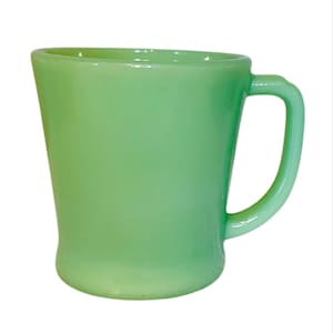 Puede incluir: Una taza vintage de vidrio verde con un asa curva. La taza tiene un acabado liso y brillante y una forma ligeramente cónica. El color es un verde suave y claro. La taza probablemente se usa para beber bebidas.