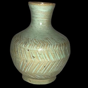 Op de afbeelding: Een kleine, lichtgroene keramische vaas met een getextureerd chevronpatroon rond de body. De vaas heeft een smalle hals en een licht uitlopende rand. De basis is een donkerdere tint groen.