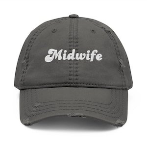 May include: A distressed gray baseball cap with the word "Midwife" in white, stylized script across the front. The cap has a curved brim and a distressed, worn look.