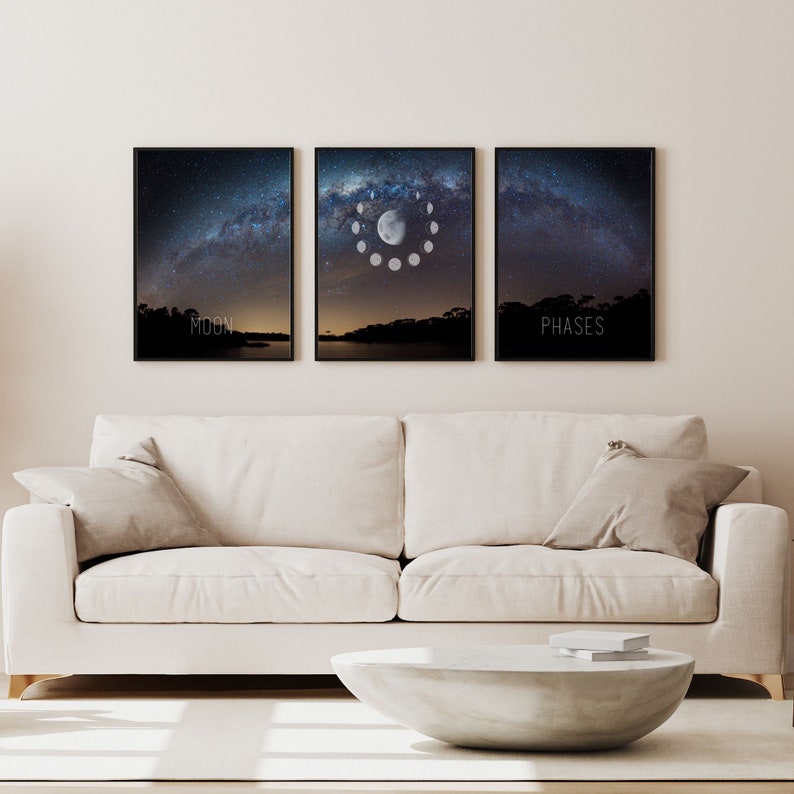 May include: Three framed art prints depicting a night sky with the Milky Way and the phases of the moon. The prints are black framed and hang above a white sofa. The text "MOON" and "PHASES" are printed on the bottom of two of the prints.