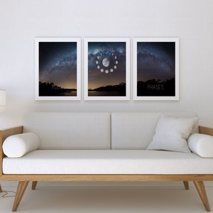 May include: Three framed art prints depicting the night sky and moon phases. The center print shows the moon's phases in a circular arrangement. The prints are in white frames and hang above a light-colored sofa. The word "MOON" is printed on the left print and "PHASES" on the right.