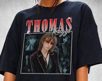 Könnte beinhalten: Schwarzes T-Shirt mit einem Grafikdesign im Vintage-Stil von Thomas Raggi, mit seinem Namen in roten und weißen Buchstaben. Die Grafik enthält mehrere Bilder von Raggi. Das T-Shirt hat einen klassischen Rundhalsausschnitt.
