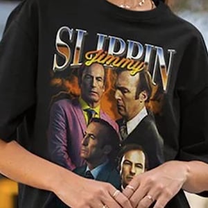 Peut inclure: T-shirt noir avec le texte "Slippin' Jimmy" dans un style vintage. Le t-shirt présente un collage d'images d'un homme en costume. Le t-shirt est de style col rond et à manches courtes.