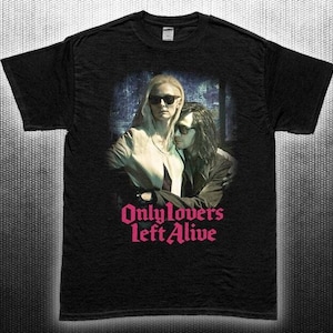 Op de afbeelding: Zwart t-shirt met een filmposterontwerp. De afbeelding toont twee mensen met een zonnebril, met de roze tekst "Only Lovers Left Alive". Het shirt is gemaakt van een donkere stof.