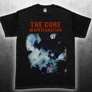 Könnte beinhalten: Schwarzes T-Shirt mit dem Bandnamen "The Cure" und dem Albumtitel "Disintegration" in roter Schrift. Das Shirt zeigt ein blau-weißes Grafikdesign. Das T-Shirt besteht aus einem weichen Material.
