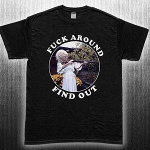 May include: Black t-shirt with a circular graphic featuring a woman in a white dress holding a rifle. The graphic is surrounded by the text "FUCK AROUND FIND OUT" in white, curved lettering.