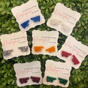 May include: Six pairs of glitter-covered megaphone earrings on white cards. Each card has the text "It's the little things Designs by Karrie". The earrings are in the colors blue, white, orange, red, burgundy, and green.