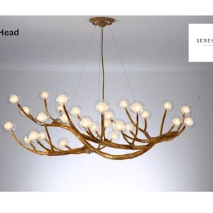 May include: A gold-toned, 28-head chandelier with a unique branch-like design and clear glass globes. The chandelier is suspended from the ceiling by a chain.