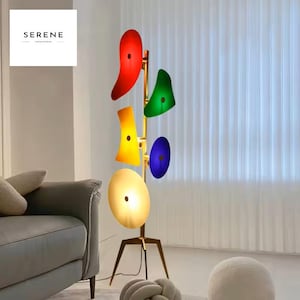 May include: A modern floor lamp with a brass finish and colorful, abstract shades in red, green, yellow, blue, and white. The lamp has a tripod base and a unique, artistic design, perfect for adding a pop of color to any room.