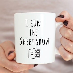 May include: White ceramic mug with a black graphic that says "I run the sheet show" with a stylized icon of a spreadsheet.