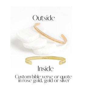 May include: A gold bangle bracelet with the text "Matthew 5:16" engraved on the inside and a bible verse engraved on the outside. The bracelet is shown on a white surface.