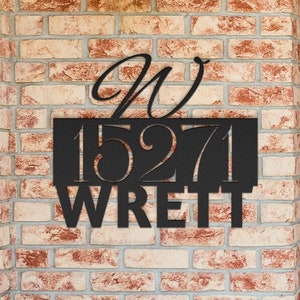 May include: Black metal house number sign with the number 1527 and the letter W above it. The sign is mounted on a brick wall.
