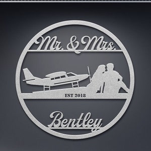 May include: A round metal sign with a silhouette of a couple and a small plane. The sign says "Mr. & Mrs. Bentley EST 2018".