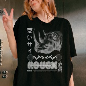 May include: Black oversized t-shirt with a graphic print of a rhinoceros, Japanese text, and the word "ROUGH" in a stylized font. The text "ESTABLISHED 2005 OKINAWA, JPN" is also printed on the shirt.