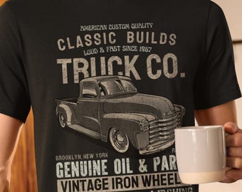 Könnte beinhalten: Schwarzes T-Shirt mit einem Vintage-Truck-Motiv und dem Text "CLASSIC BUILDS TRUCK CO.". Das T-Shirt enthält auch den Text "GENUINE OIL & PAR" und "VINTAGE IRON WHEEL". Eine Person trägt das T-Shirt und hält einen weißen Becher.