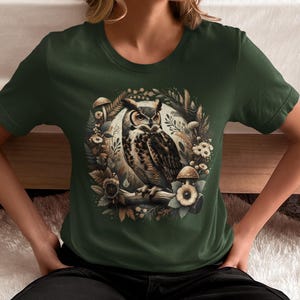 May include: A green t-shirt featuring an illustration of a brown and white owl surrounded by mushrooms and leaves.